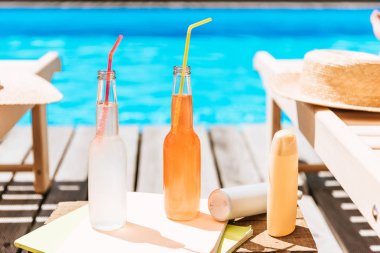 close-up view of bottles with summer drinks, sunscreen and chaise lounges at swimming pool clipart