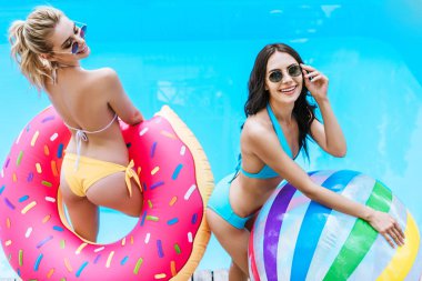 bikini ve şişme top ve halka yüzme havuzunda tutan güneş gözlüğü mutlu genç kadınların yüksek açılı görünüş  