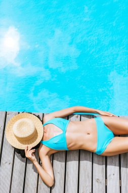 top view of young woman in bikini and straw hat on face lying near swimming pool  clipart