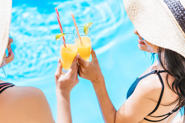 обрезанный снимок молодых женщин в купальниках и шляпах, держащих бокалы с освежающими напитками в бассейне
 