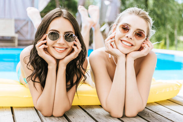 beautiful young women lying on inflatable mattress and smiling at camera at poolside