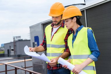 professional architects in helmets working with blueprints on roof clipart