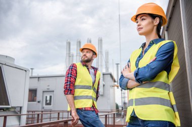 professional engineers in safety vests and helmets posing on roof