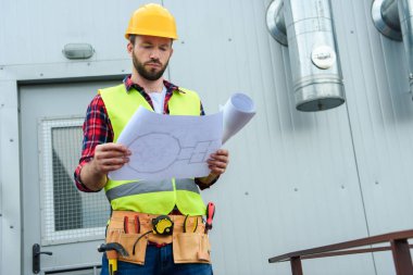 male architect in safety vest and helmet working with blueprints clipart