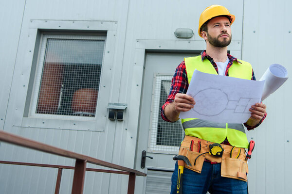 male professional engineer in safety vest and helmet working with blueprints