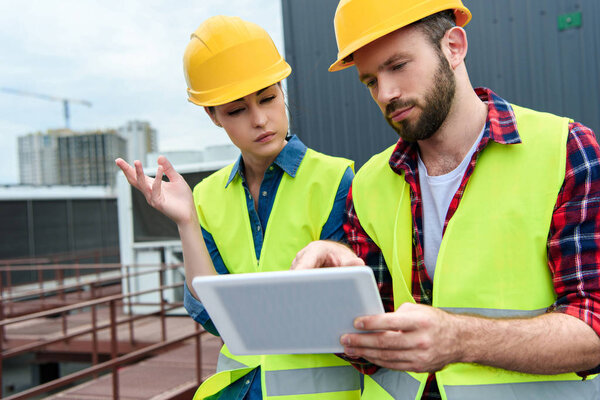 thoughtful architects in helmets using digital tablet