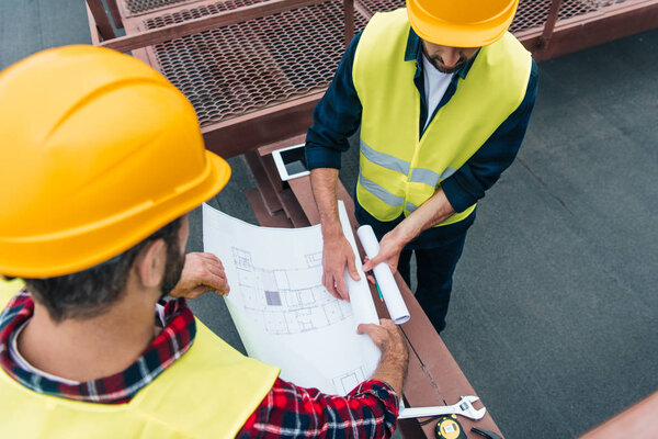 overhead view of architects in safety vests and helmets working with blueprints
