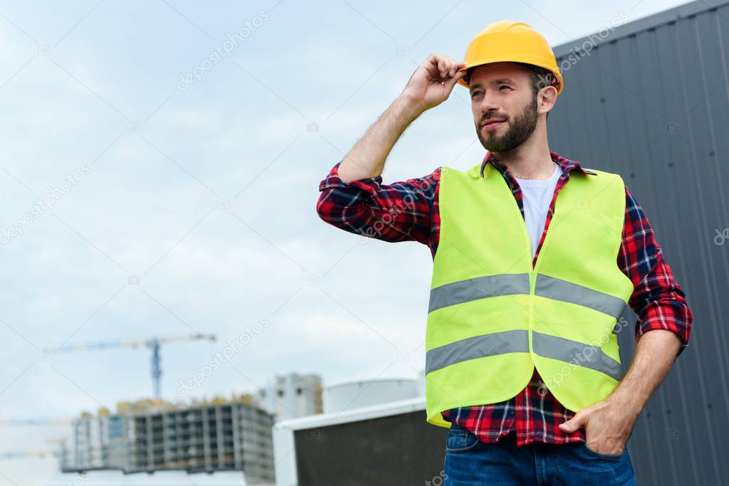 professional confident engineer in safety vest and helmet posing on roof