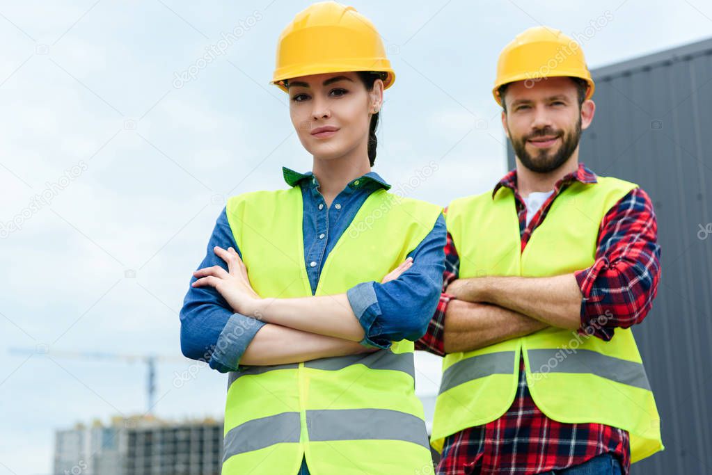 professional architects posing in helmets and safety vests with crossed arms