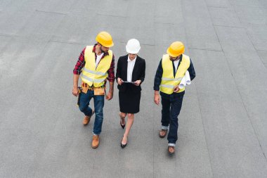 overhead view of female architect and male workers in helmets with clipboard and blueprints clipart