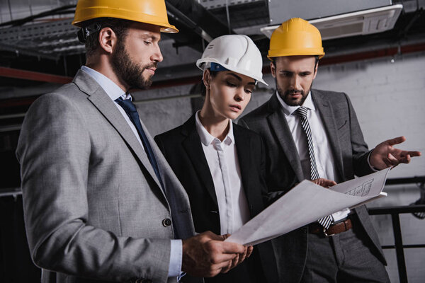 architects and engineers in suits and hardhats working with blueprint on construction