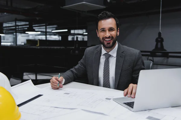 Glimlachend Mannelijke Architect Werken Met Blauwdrukken Laptop — Stockfoto