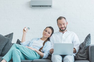 couple turning on air conditioner during the summer heat while using laptop clipart