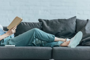 cropped view of woman relaxing on sofa and reading book  clipart
