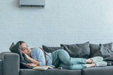 woman sleeping on sofa with book and air conditioner on wall clipart