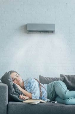 woman sleeping on couch with book and air conditioner blowing on her clipart