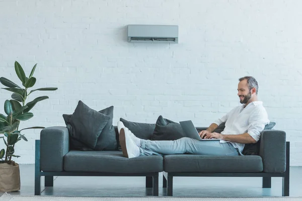 Knappe Man Werken Met Laptop Bank Met Airconditioner Muur Thuis — Stockfoto