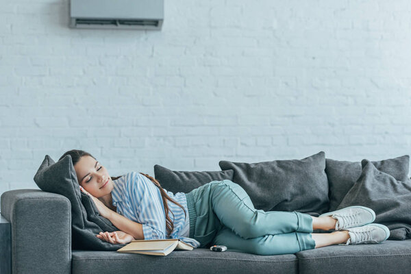 woman sleeping on sofa with book and air conditioner on wall