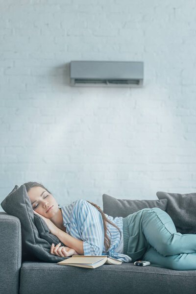 woman sleeping on couch with book and air conditioner blowing on her