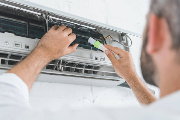 selective focus of repairman cleaning air conditioner with brush