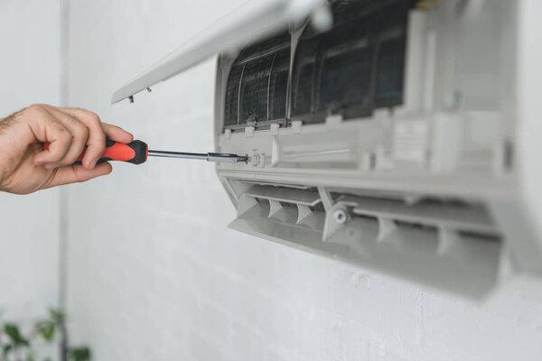 partial view of male worker repairing air conditioner with screwdriver