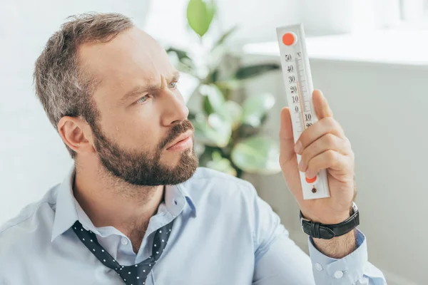 confused businessman in hot office looking at thermometer