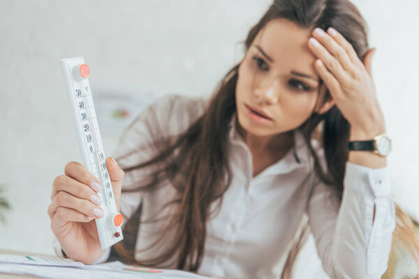 selective focus of businesswoman in hot office looking at thermometer