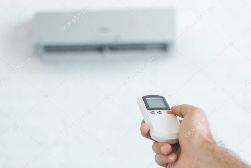 cropped view of man turning on air conditioner with remote control, selective focus
