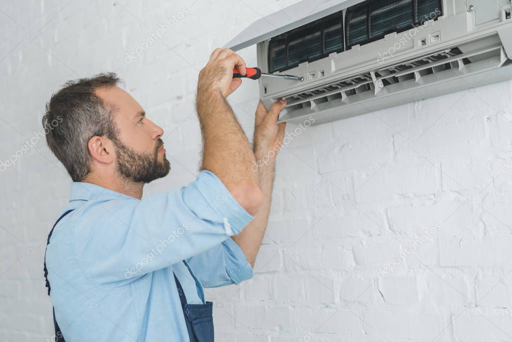 Repairman fixing air conditioner with screwdriver at summer heat