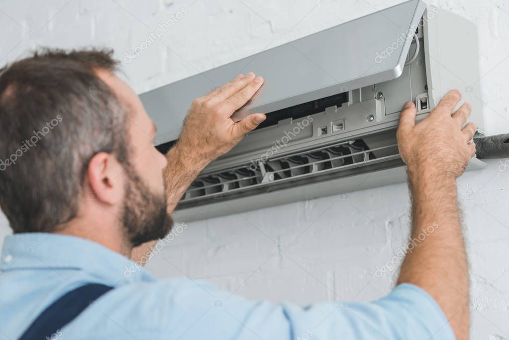 Male worker fixing air conditioner at home