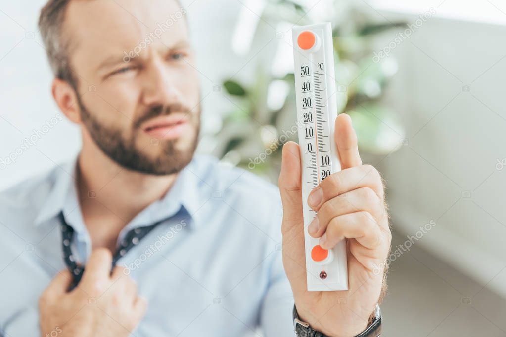 selective focus of businessman in hot office looking at thermometer