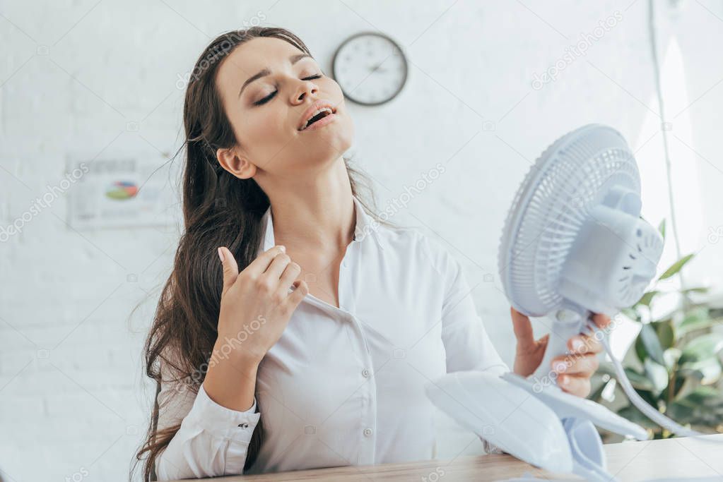 businesswoman conditioning herself with electric fan in office