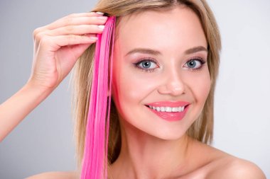happy young woman applying pink clip-on hair strand isolated on grey clipart