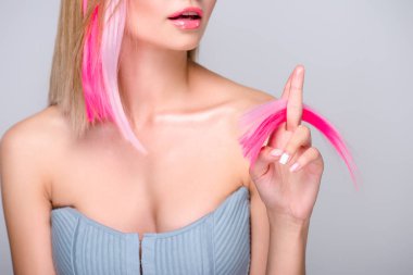 cropped shot of young woman holding cut colorful hair strands and looking at camera isolated on grey clipart