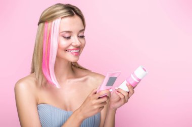 happy young woman with colorful hair strands holding hair treatments isolated on pink clipart