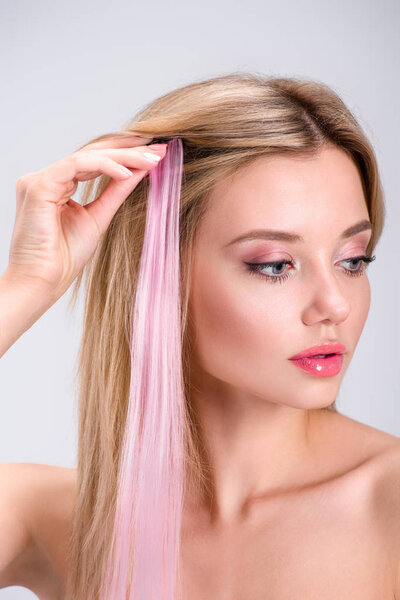 attractive young woman applying pink clip-on hair strand isolated on grey