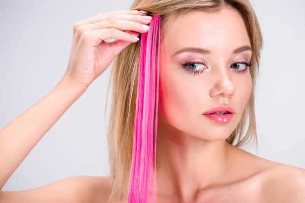 attractive young woman applying pink clip-on hair strand isolated on grey