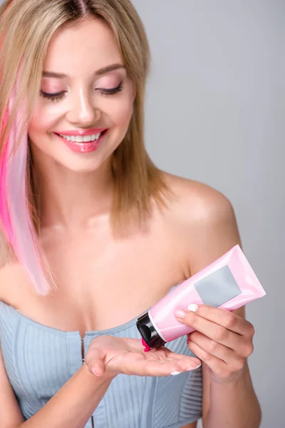 happy young woman pouring pink coloring hair tonic on hand isolated on grey