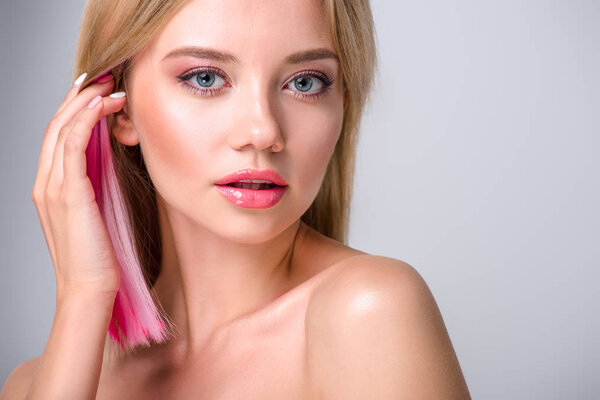 close-up portrait of beautiful young woman putting colored hair behind ear and looking at camera isolated on grey