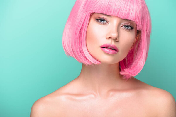 attractive young woman with pink bob cut and stylish makeup looking at camera isolated on turquoise