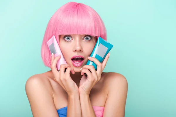 shocked young woman with tubes of coloring hair tonics looking at camera isolated on turquoise
