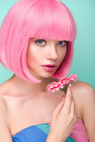 close-up portrait of beautiful young woman with pink bob cut holding flower and looking at camera isolated on turquoise