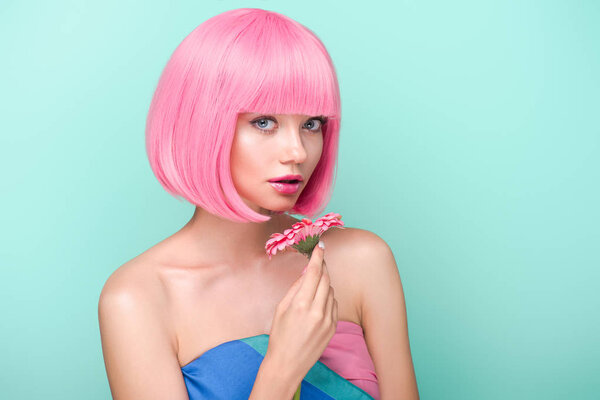 beautiful young woman with pink bob cut holding flower and looking at camera isolated on turquoise