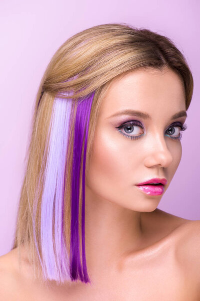 close-up portrait of attractive young woman with stylish makeup and purple hair strands looking at camera isolated on purple