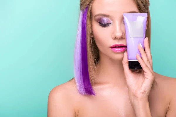 beautiful young woman with colorful hair holding hair tonic tube isolated on blue