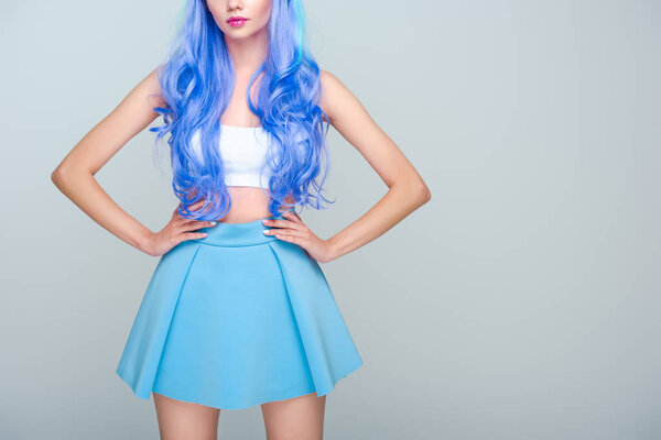 cropped shot of young woman with curly bright blue hair and arms akimbo isolated on grey