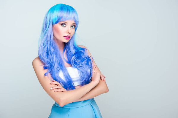 beautiful young woman with bright blue hair and crossed arms looking at camera isolated on grey