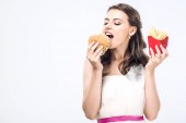 Hangry mladá nevěsta ve svatebních šatech jíst hamburger a hranolky, izolované na bílém