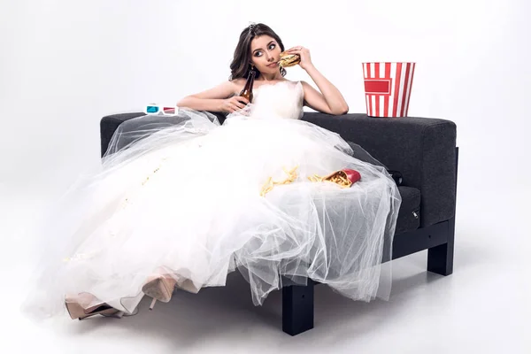 ビールと白のジャンク フードでソファの上に座ってのウェディング ドレスで悲しい若い花嫁 — ストック写真