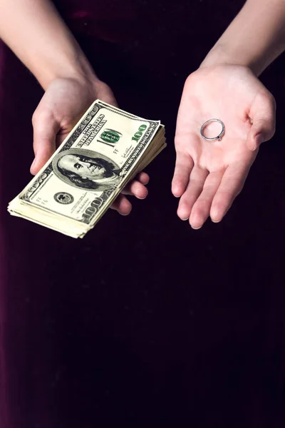 cropped shot of woman holding cash and wedding ring, marriage of convenience concept
